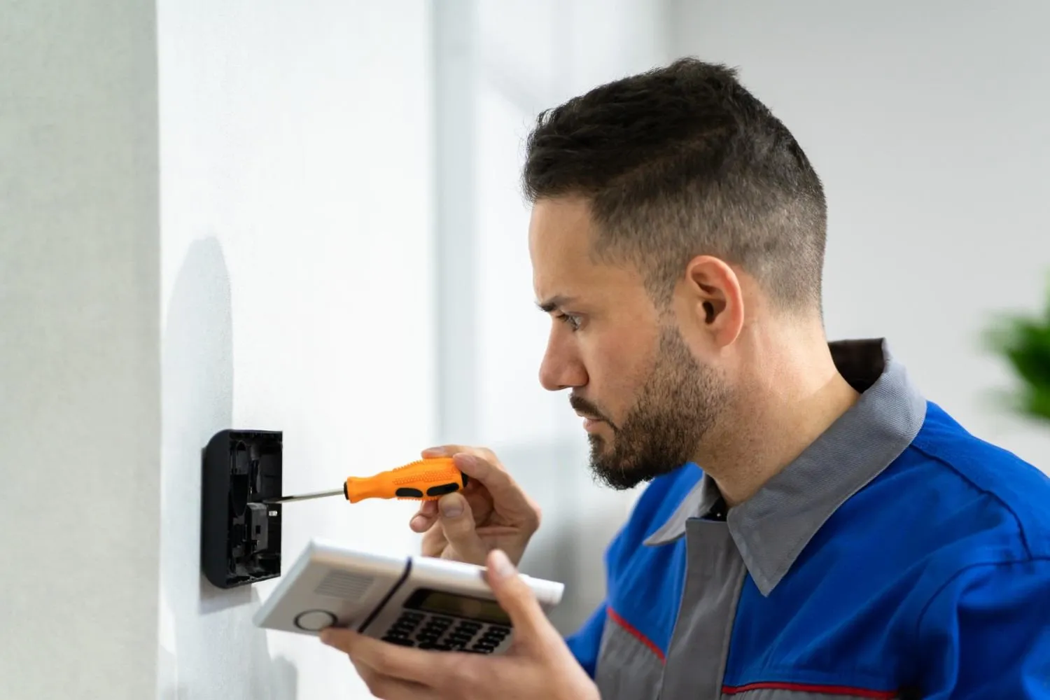 Contractor repairing a wall thermostat with a screwdriver